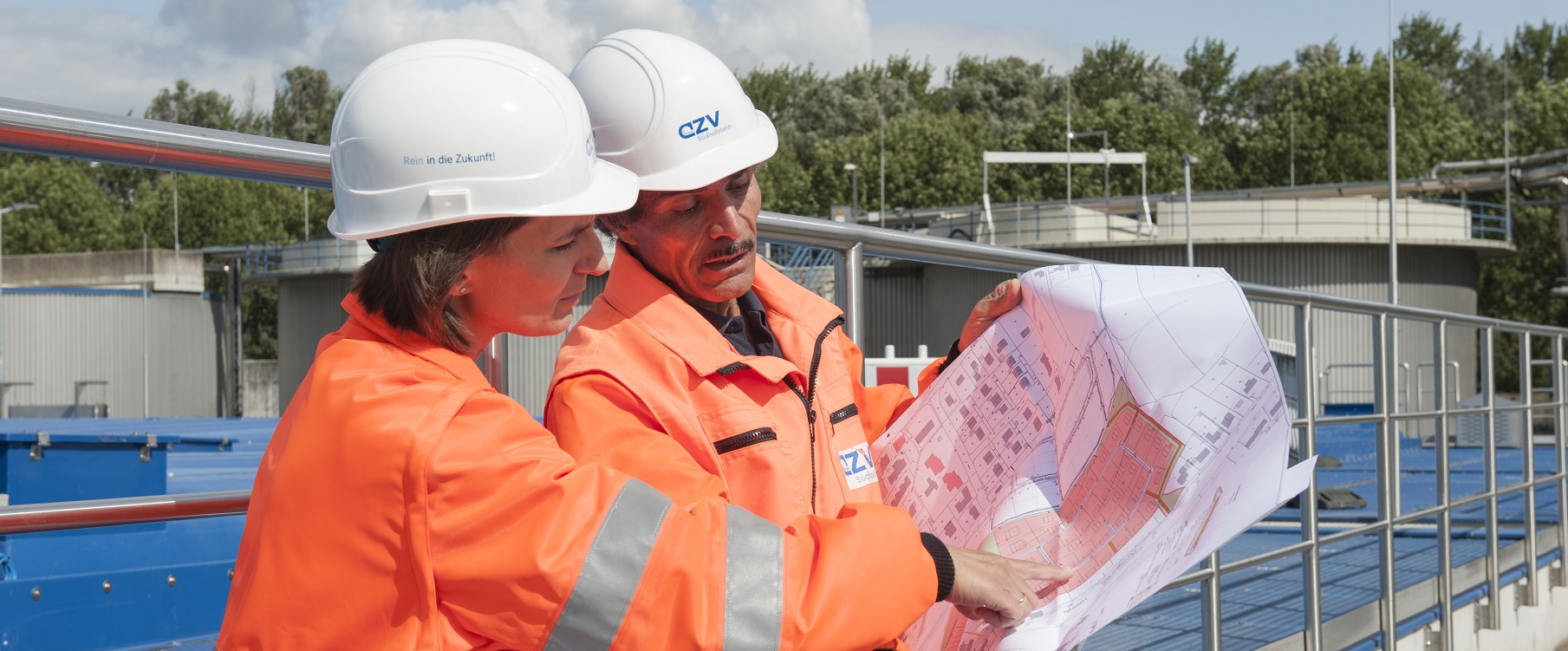 Zwei Mitarbeitende des AZV in orangenen Warnwesten schauen gemeinsam auf eine Bauzeichnung